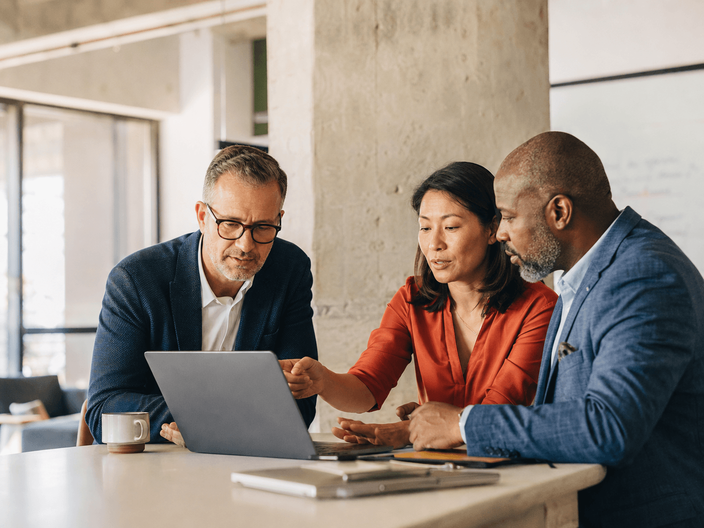 Technology consultants and a client leader collaborating around a laptop